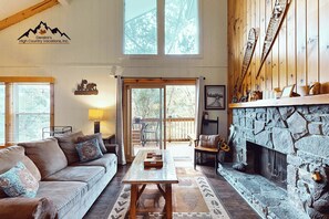 Una sala de estar acogedora con chimenea de piedra, un sofá, una mesa de centro y un ventanal con vistas a una terraza.