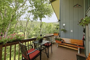 A wooden deck with a table and chairs, surrounded by greenery and a view of a forested area. - Slopeside & Creekside Sugar Mountain Condo (Sugar Mountain)