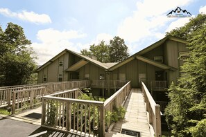 A two-story lodge with a wooden deck and stairs leading to the entrance. - Slopeside & Creekside Sugar Mountain Condo (Sugar Mountain)