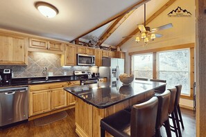A modern kitchen with wooden cabinets, stainless steel appliances, and a central island with bar stools. - Slopeside & Creekside Sugar Mountain Condo (Sugar Mountain)