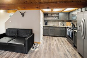 Eine kompakte Küche mit modernen Geräten, ein schwarzes Ledersofa und eine Holzbalkendecke.