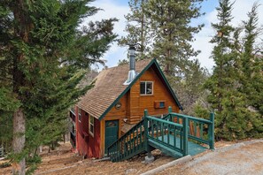 Una pequeña cabaña de madera con techo a dos aguas, una chimenea y una escalera verde que lleva a la entrada.