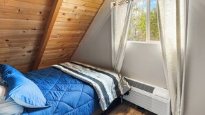Una habitación pequeña con techo inclinado, una cama, un ventanal con cortinas y un calefactor en la pared.