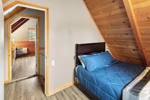 Ein Schlafzimmer mit schrägen Wänden, einem Bett mit blauer Bettwäsche und einem sichtbaren Badezimmer mit Dusche.