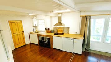 Une cuisine avec un plancher en bois, un four encastré, un évier et une fenêtre avec des rideaux.