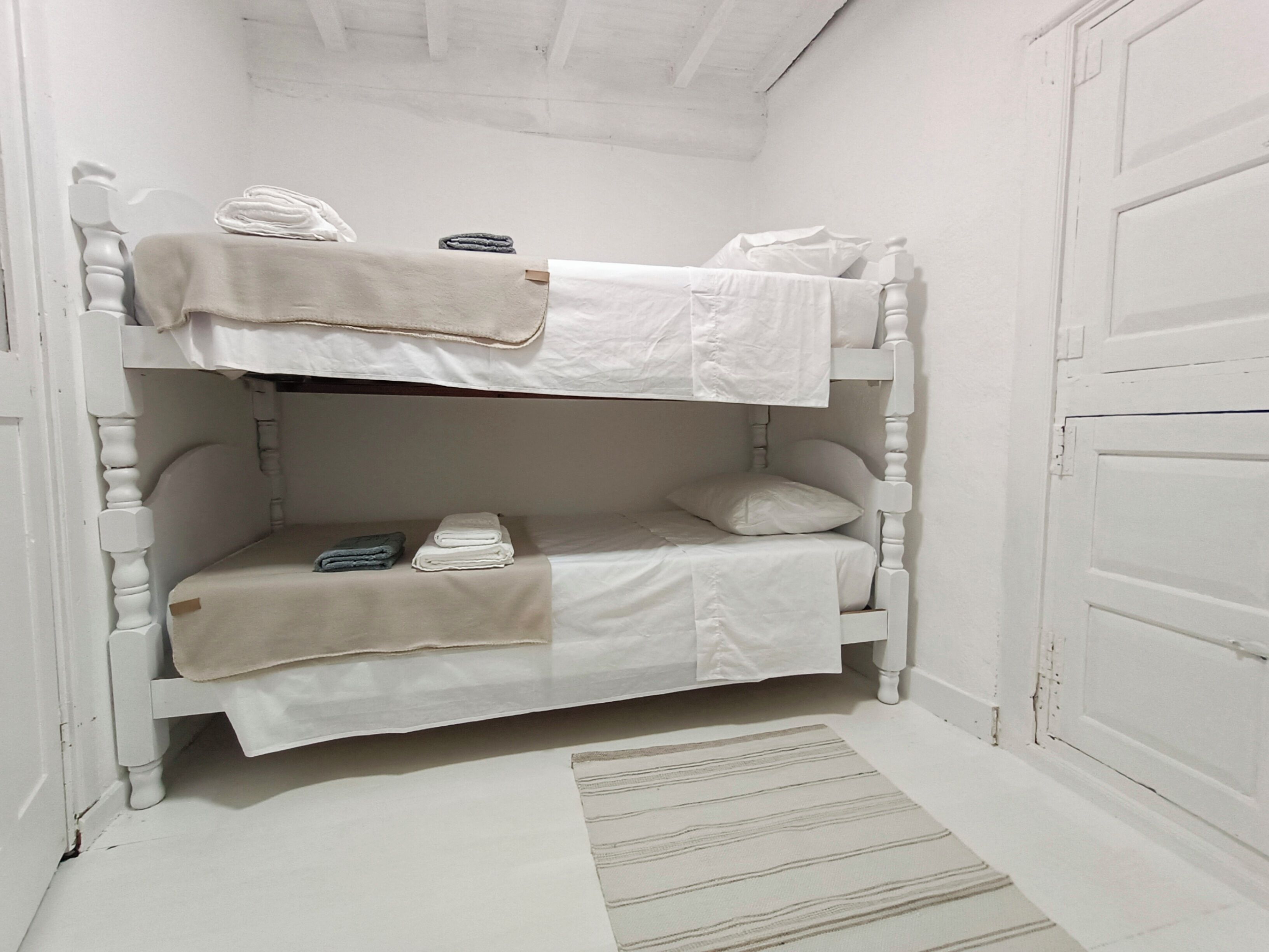 Een stapelbed met witte beddengoed en een gestreept vloerkleed.