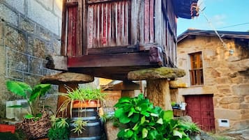 Un bâtiment rustique en bois, avec une porte rouge, entouré de verdure et de plantes en pot.