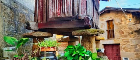 A rustic wooden building with a red door, surrounded by greenery and potted plants.