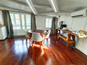 A dining area with a wooden table and chairs, a kitchen area with a microwave, and large windows with curtains. - A Casiña Do Río el encanto del rural. Bienvenidas mascotas. (Santa Baia Berredo A Bola)