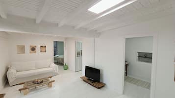 Un salon moderne avec un canapé blanc, une table basse, un téléviseur à écran plat et un plancher en bois.