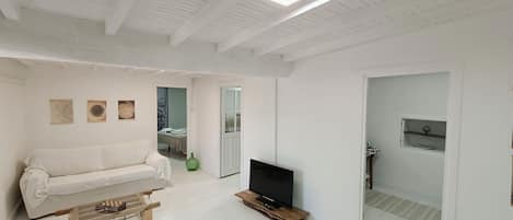 A modern living room with a white sofa, a coffee table, a flat-screen TV, and a wooden floor.