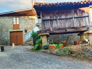 A rustic stone building with a wooden porch, a stone wall, and a paved ground. - A Casiña Do Río el encanto del rural. Bienvenidas mascotas. (Santa Baia Berredo A Bola)