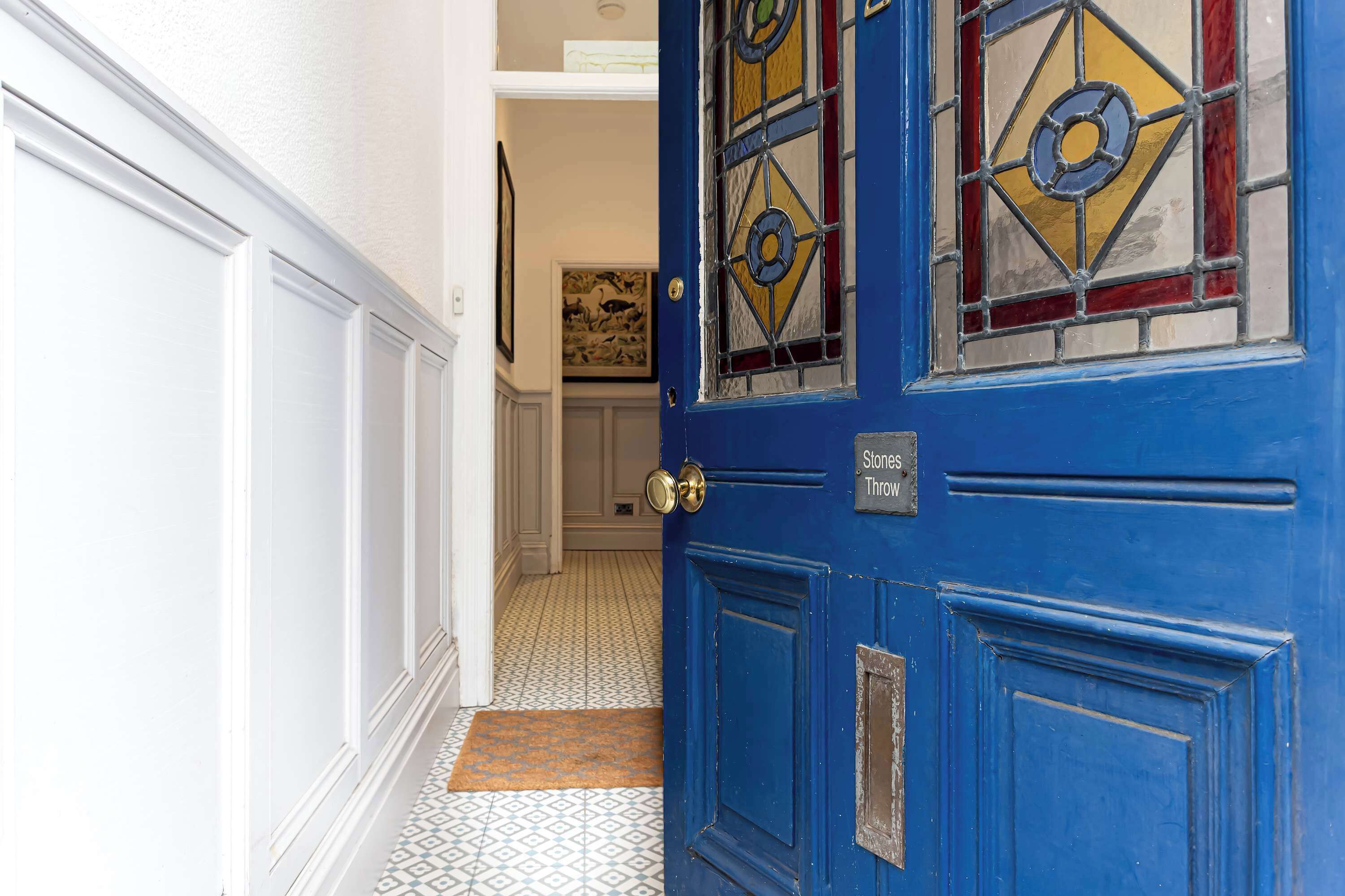 A blue door with a sign reading 'Stones Throw' and a patterned floor leading to a room with a framed picture on the wall.