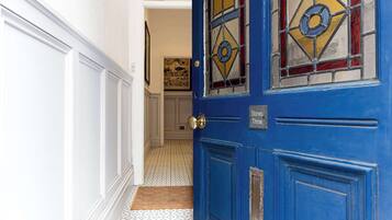 A blue door with a sign reading 'Stones Throw' and a patterned floor leading to a room with a framed picture on the wall.