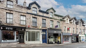 A row of traditional stone buildings with various shops, including a barbershop and a property sales office. - Charming 2BR Flat on Grange-Over-Sands High Street (Grange over Sands)