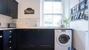A compact kitchen with dark cabinetry, a built-in washing machine, a window with a view, and a bulletin board with travel brochures.