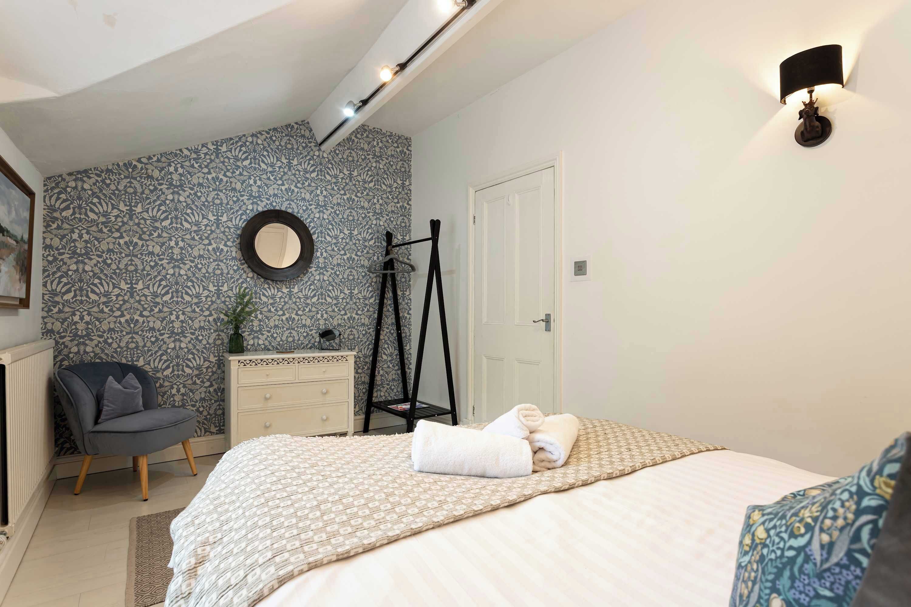A bedroom with a bed, a chair, a dresser, and a mirror on the wall.