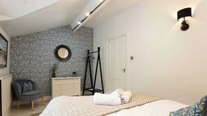 A bedroom with a bed, a chair, a dresser, and a mirror on the wall. - Charming 2BR Flat on Grange-Over-Sands High Street (Grange over Sands)