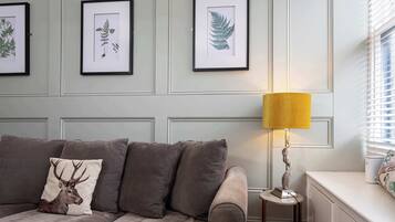 A room with a grey sofa, a lamp, and framed botanical prints on the wall.