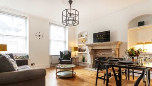 A living room with a fireplace, a dining area with a table and chairs, a sofa, and a coffee table. - Charming 2BR Flat on Grange-Over-Sands High Street (Grange over Sands)