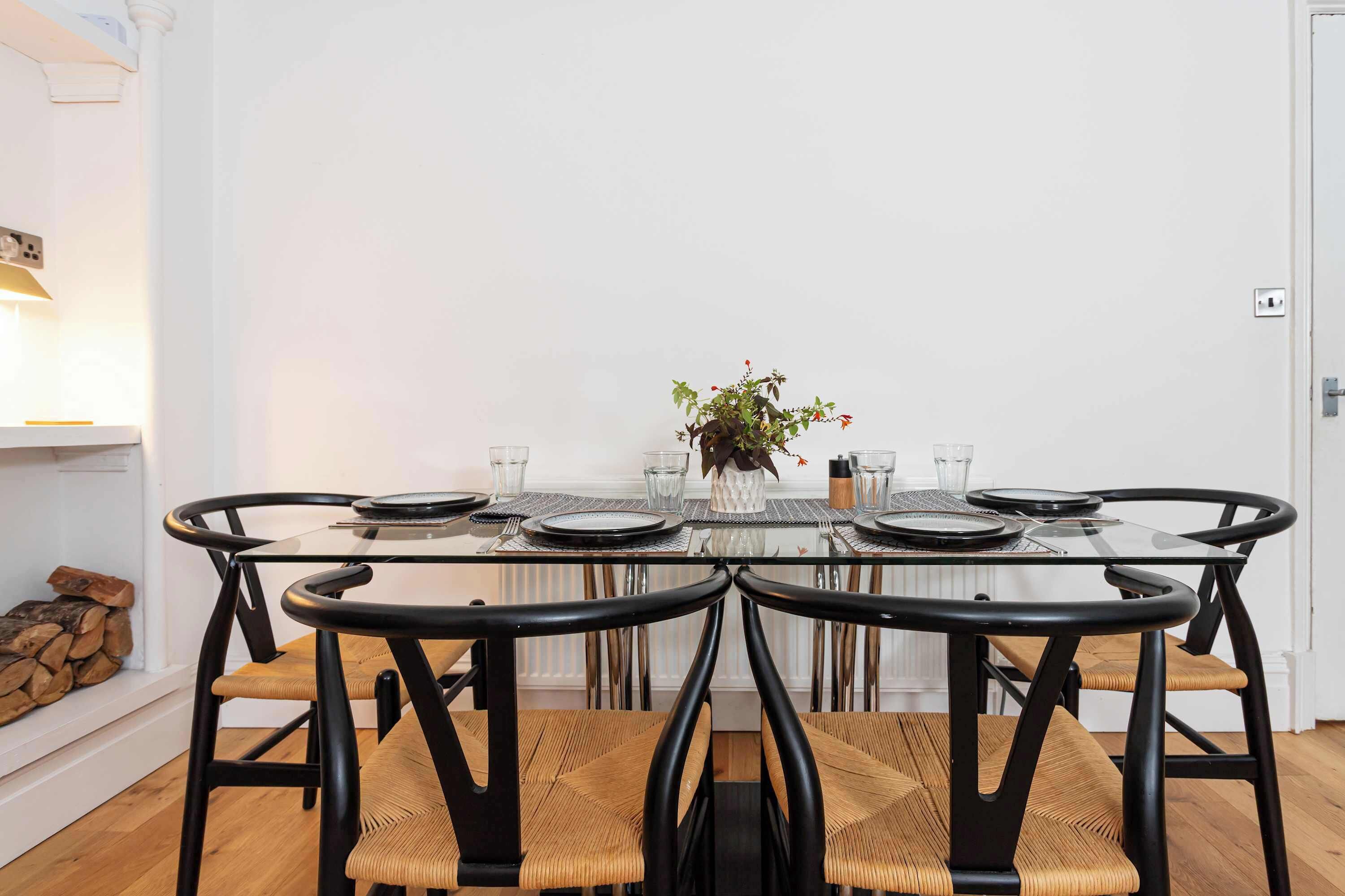 A dining area with a glass table, black chairs, and a white wall.