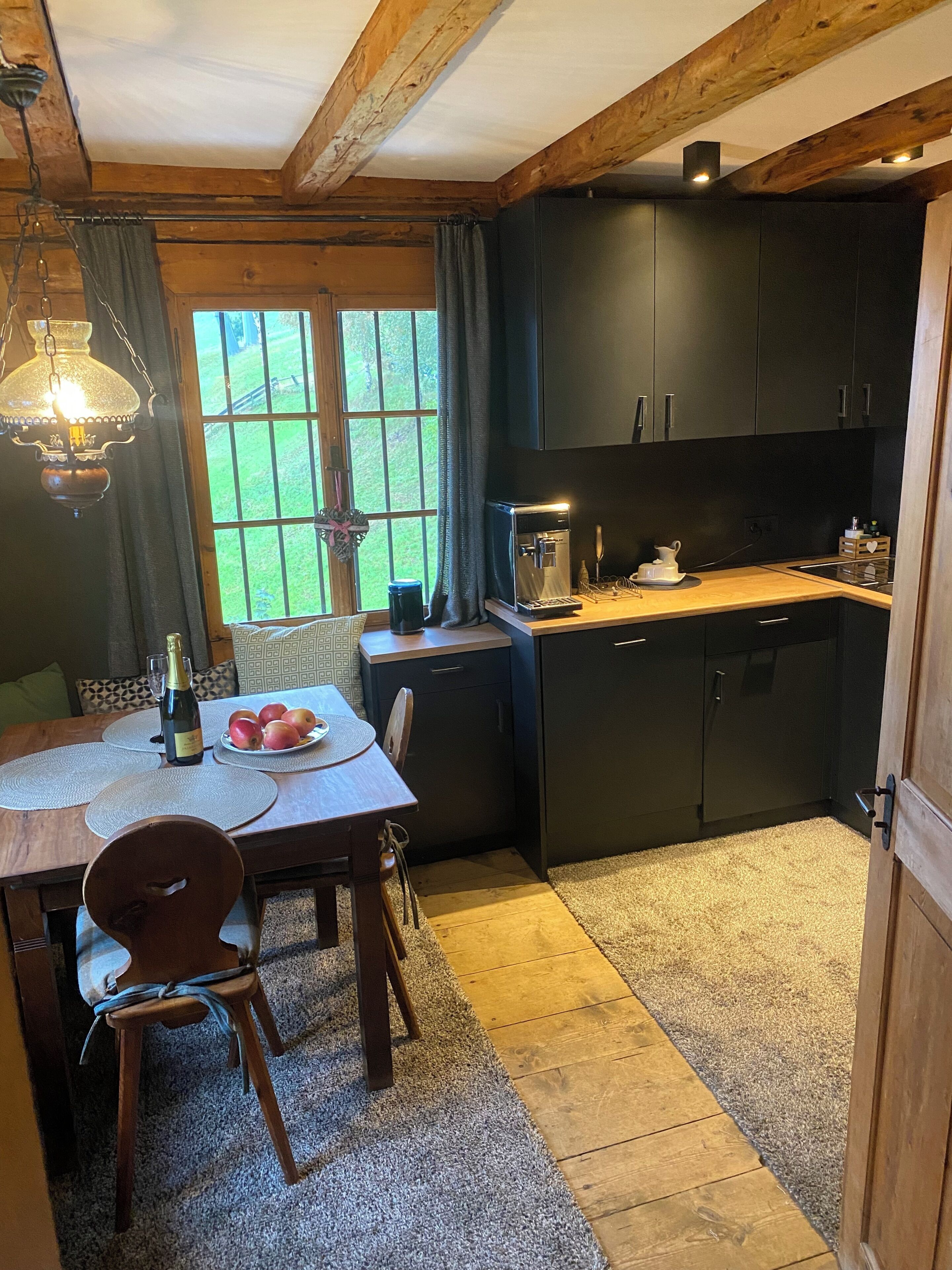 Een gezellige keuken met houten balken, een eettafel met stoelen, een koffiezetapparaat en uitzicht op het omliggende landschap.