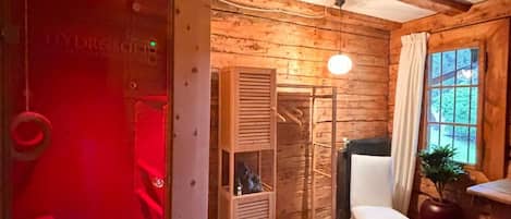 Una habitación con paredes de madera, una puerta iluminada con luz roja, una silla blanca, una mesa y una ventana con vistas.