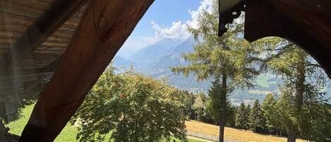 A wooden structure with a view of a mountainous landscape, a bench, and flowering plants.
