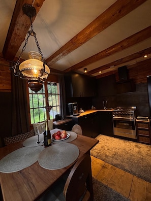 A wooden interior with a dining table set for two, a chandelier, and a kitchen area with modern appliances.