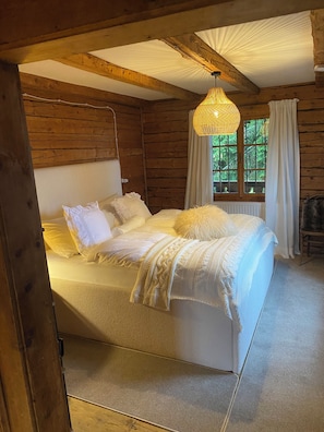 A wooden cabin bedroom with a bed, a hanging light fixture, and a window with curtains.