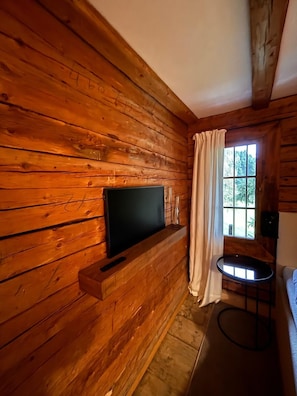 A wooden cabin interior with a television mounted on a wall, a small table, and a window with curtains. - Ifinger Mountain Chalet—an exclusive vacation home just for you. Modern design, quiet location. (Schenna)