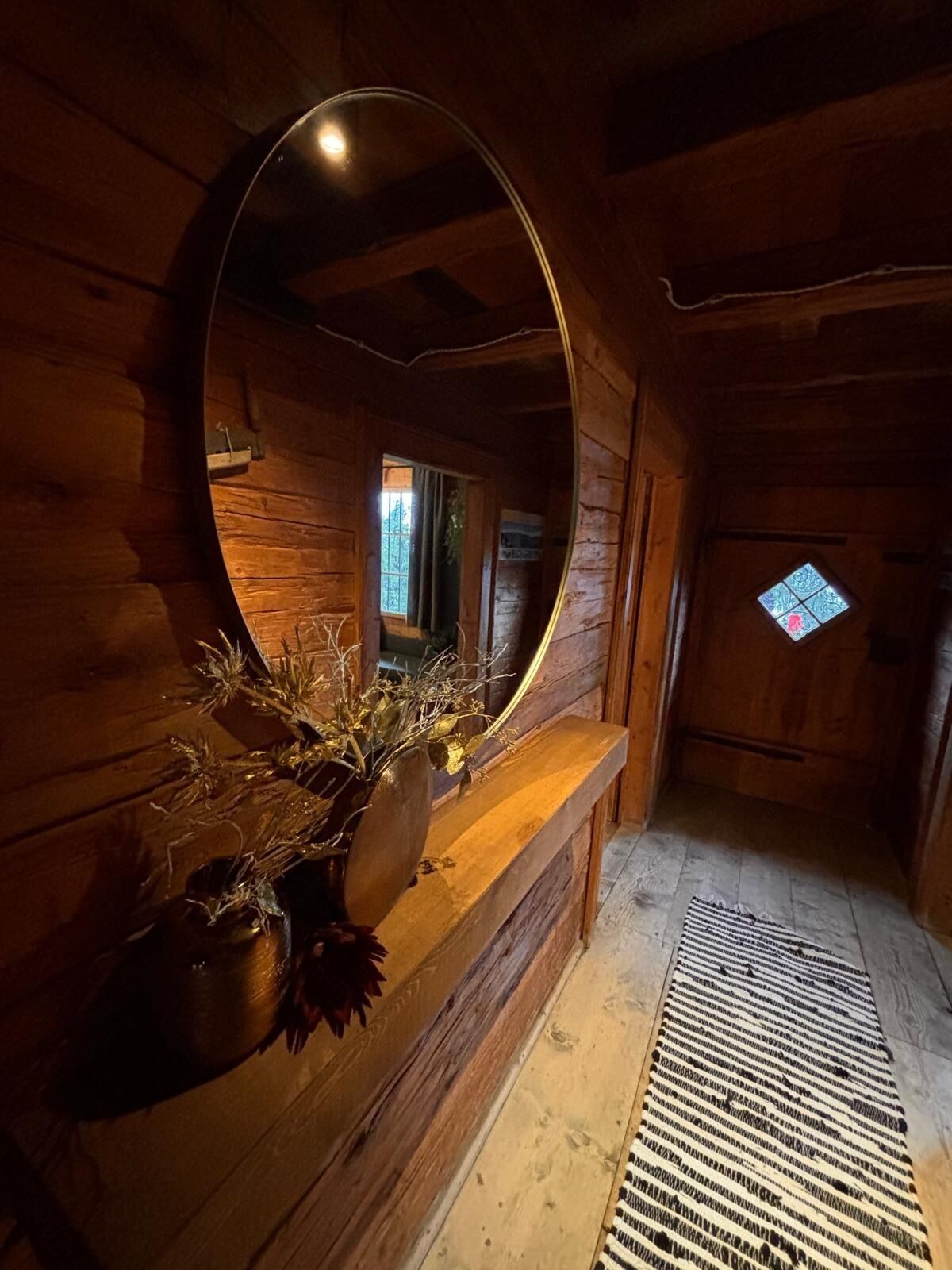 Un intérieur en bois avec un grand miroir, un banc en bois et une petite fenêtre.