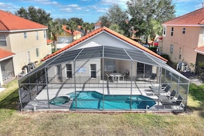 A covered outdoor swimming pool with a glass enclosure, surrounded by a lawn and residential buildings. - Casa Sevilla | 4 BD | Sleeps 8 | Pool/Spa | Disney (Davenport)