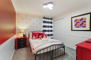 Een slaapkamer met een bed, nachtkastje, dressoir, een muurdecoratie met het thema Mickey Mouse, een lijst met een afbeelding van Mickey Mouse en een gestreept gordijn.
