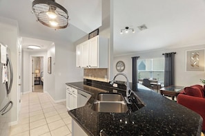 A modern kitchen with a black granite countertop, stainless steel sink, and white cabinetry. - Casa Sevilla | 4 BD | Sleeps 8 | Pool/Spa | Disney (Davenport)
