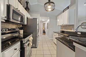 A modern kitchen with stainless steel appliances, white cabinetry, and a black countertop. - Casa Sevilla | 4 BD | Sleeps 8 | Pool/Spa | Disney (Davenport)