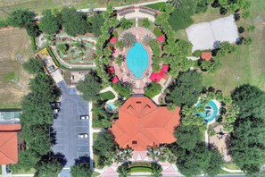 Luchtbeeld van een resort met een centraal gelegen zwembad, een parkeerplaats en omliggend groen.