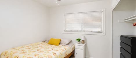 A bedroom with a bed, a nightstand, a ceiling fan, a window with blinds, and a dresser.