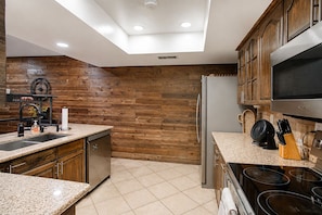 A modern kitchen with wooden wall paneling, a stainless steel refrigerator, and a granite countertop.