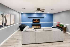 A living room with a gray sectional sofa, a black bean bag, a wooden entertainment center, and a ceiling fan.