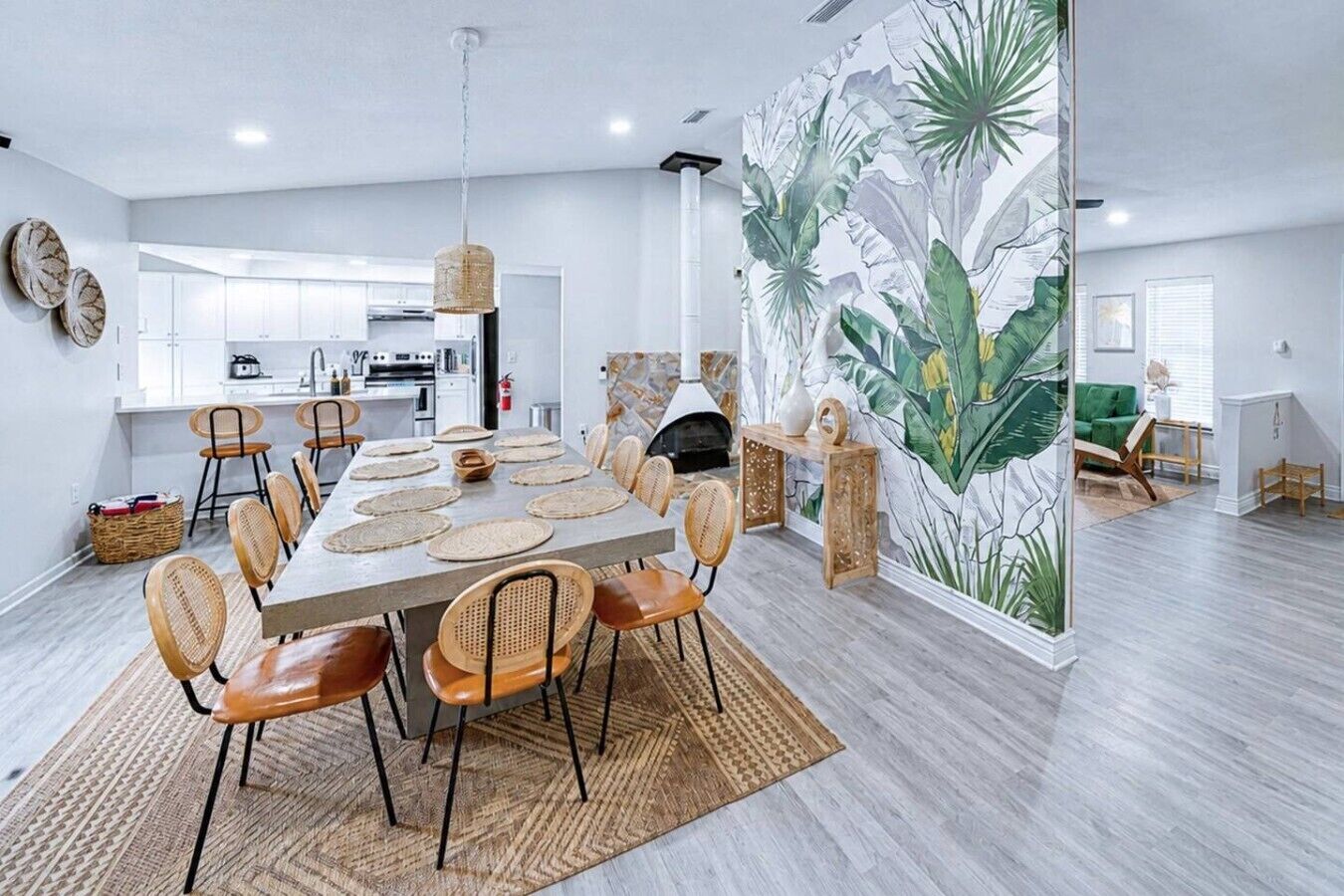 A modern dining area with a long table, wicker chairs, and a decorative wall mural.