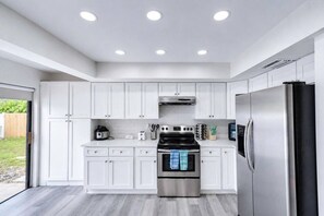 A modern kitchen with white cabinets, stainless steel appliances, and a grey wooden floor. - Palm Harbor Pool 4BR | Hot Tub + BBQ + Game Room (Palm Harbor)