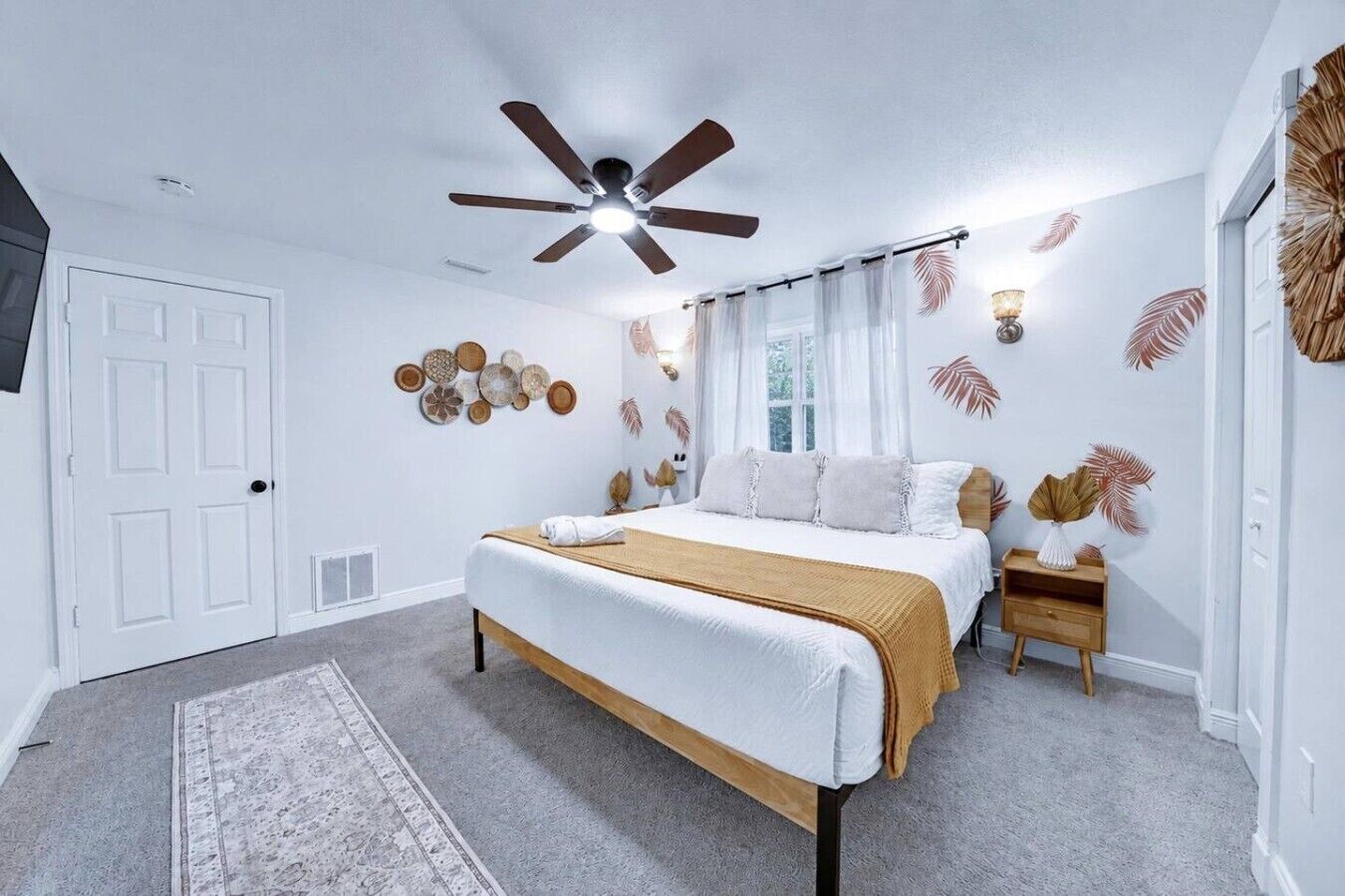 A bedroom with a bed, a ceiling fan, a nightstand, and a wall with decorative elements.