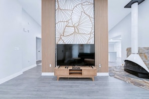 A modern living room with a large flat-screen TV mounted on a wooden stand, a stone fireplace, and a minimalist design. - Palm Harbor Pool 4BR | Hot Tub + BBQ + Game Room (Palm Harbor)