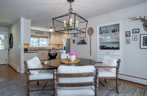 A dining area with a round table, two chairs, a chandelier, and a wall-mounted shelf with glassware. - Sun Valley Sanctuary in Highly Sought After Location (Sun Valley)