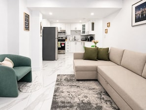 En moderne stue med en sofa, en grøn lænestol og en løber med marmor-mønster.