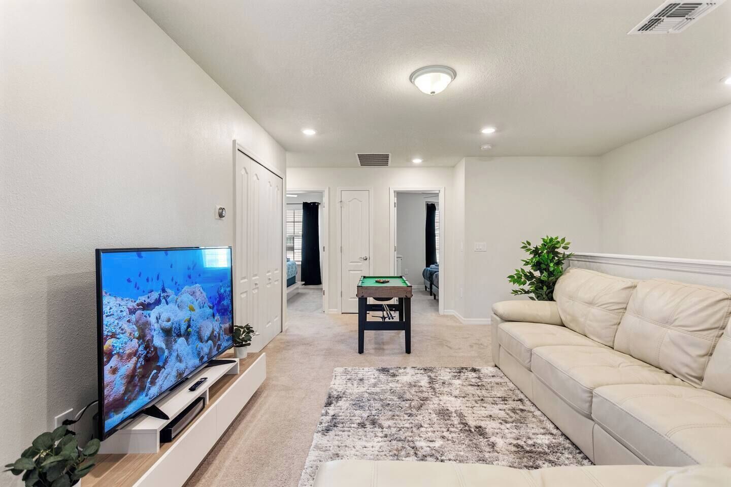 A living room with a television, a sofa, a pool table, and a hallway leading to other rooms.