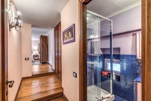 A hallway with wooden flooring, a glass shower enclosure, and a framed picture on the wall. - Old Government Vacation Home (Roma)