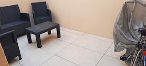 A small patio area with two wicker chairs and a table, a covered bicycle, and a tiled floor. - Vacation Home in Cayeux-sur-mer (Cayeux-sur-Mer)