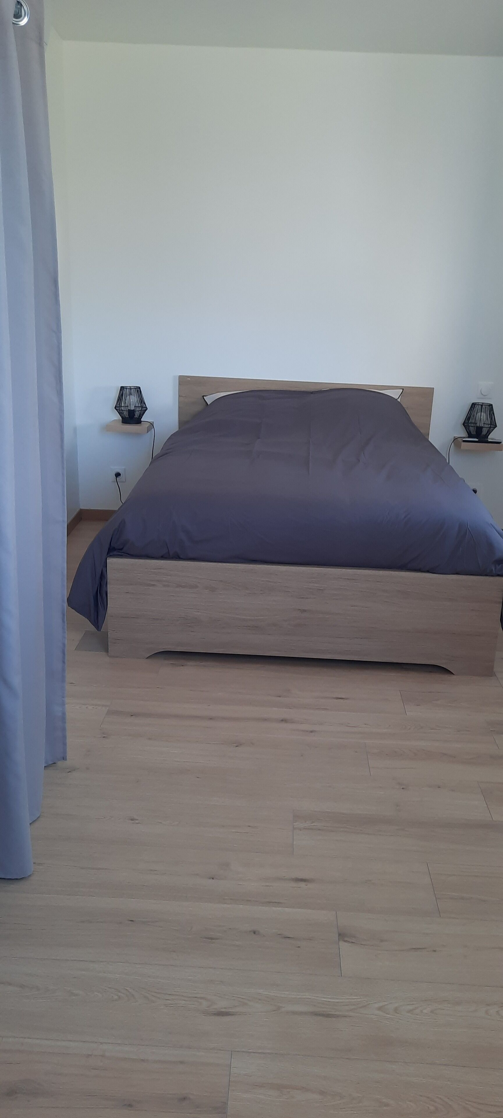 A single bed with a wooden frame and a dark-colored mattress in a room with light-colored walls and wooden flooring.